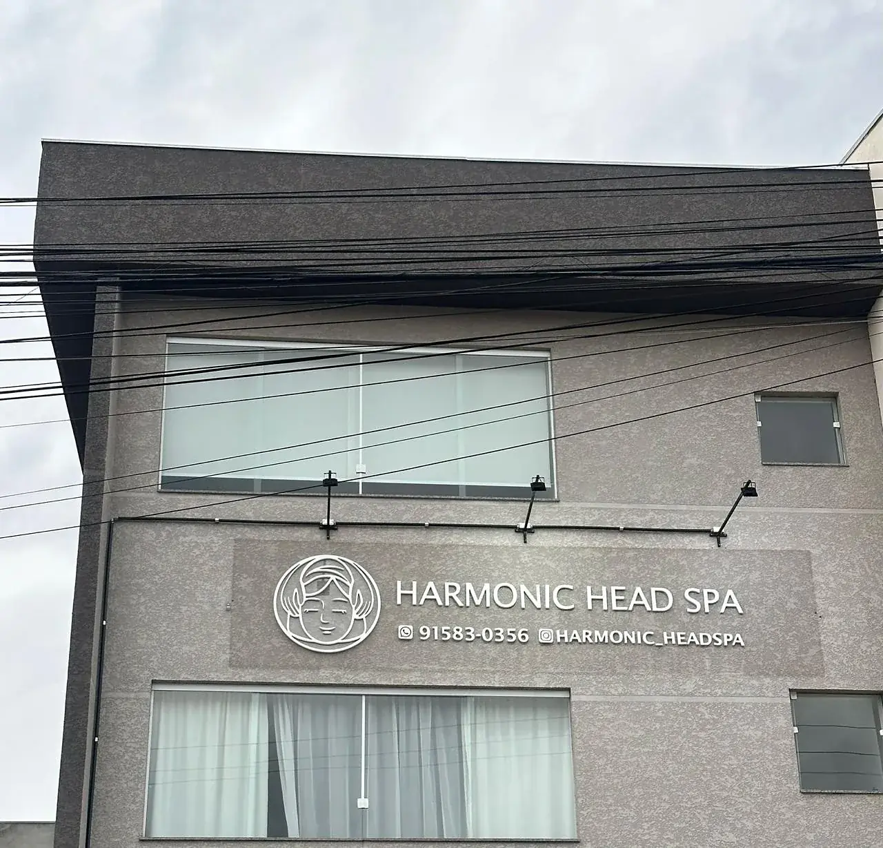 Fachada do prédio do Harmonic Head Spa com a logo, o telefone e o Instagram na parede